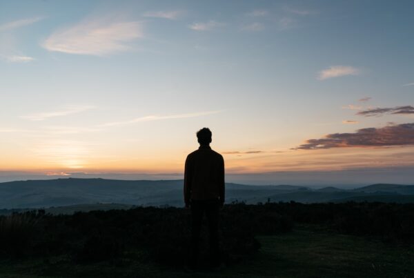 silhouette of man standing on green grass field during sunset